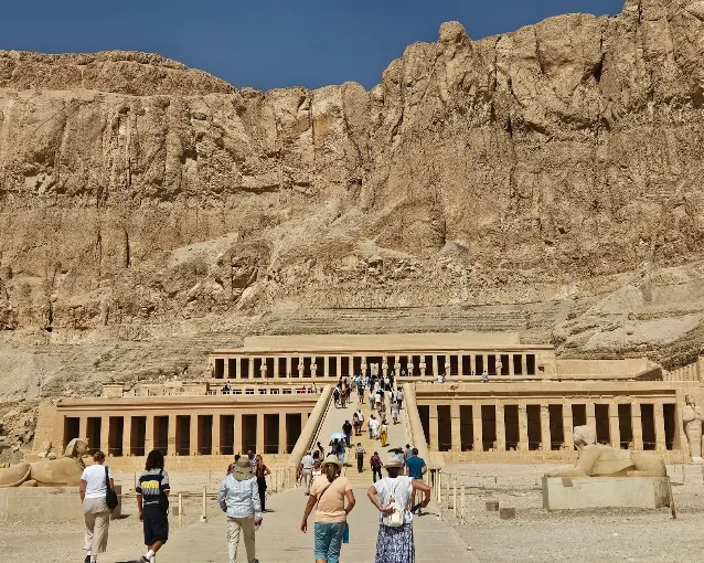 Small group of travelers walking up to the terraced Temple of Hatshepsut beneath desert cliffs on a guided tour of Egypt